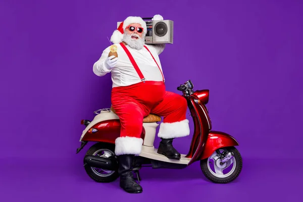 Wesołych Świąt. Pełne zdjęcie człowieka Santa siedzi na napój alkoholowy motorower i vintage magnetofon na ramię nosić specyfikacje i kostium odizolowane fioletowe tło — Zdjęcie stockowe