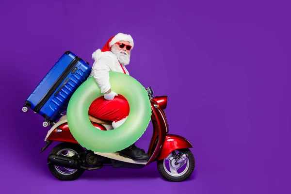 Full size profile photo of santa man going to meet newyear at tropics leaving by moped hold life buoy big bag wear specs and costume isolated purple background