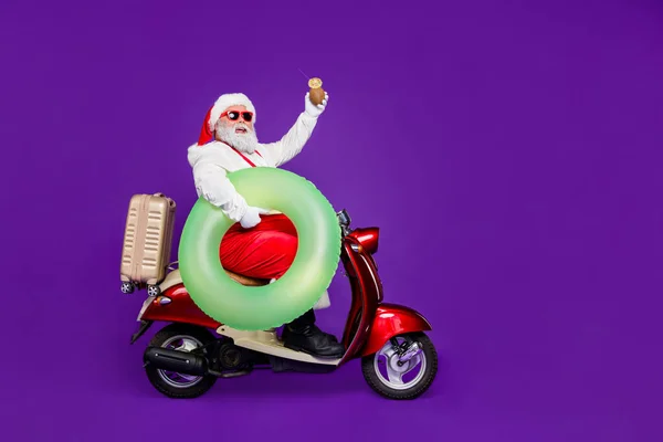 Foto de cuerpo completo del hombre de santa va a cumplir un nuevo año en los trópicos dejando frío diciembre en bicicleta mantenga boya de la vida y beber desgaste especificaciones y traje aislado fondo púrpura — Foto de Stock