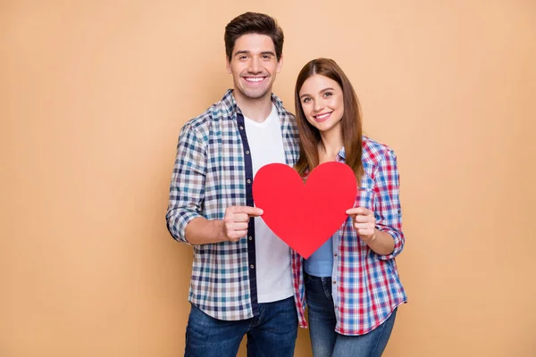 Retrato de pareja romántica positiva celebrar tarjeta de papel rojo corazón mostrar símbolo de sus sentimientos usar cuadros a cuadros traje de estilo casual aislado sobre fondo de color pastel —  Fotos de Stock