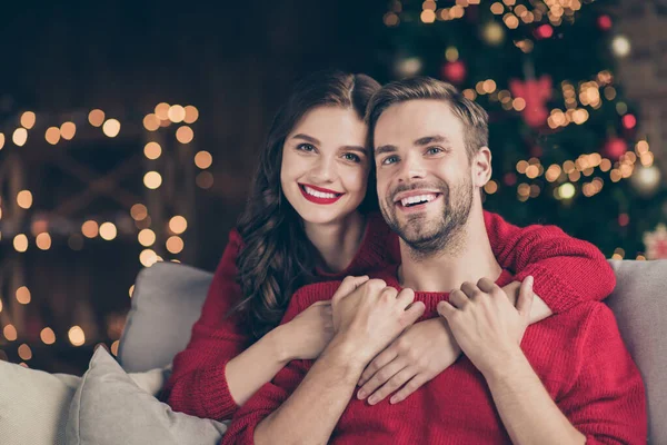 Zbliżenie zdjęcie uroczej pary spędzającej Holly Christmas Eve w urządzone światła girlandy pokój w pobliżu nowyrok choinki piggyback siedzi przytulna sofa w pomieszczeniach w czerwonych pulowerów — Zdjęcie stockowe