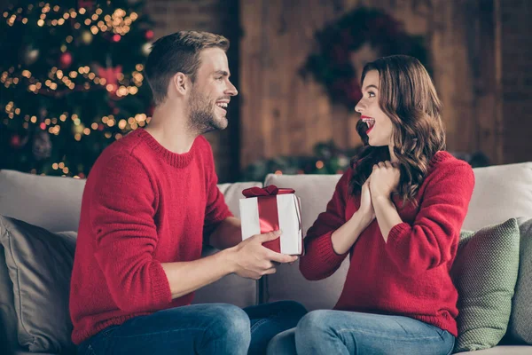 To dla mnie. Profil zdjęcie podekscytowanych para dzieląc się prezenty X-mas spędzać czas w urządzone światła girlandy pokój siedzi przytulny na kanapie w pomieszczeniach nosząc czerwone dzianiny pulowery — Zdjęcie stockowe