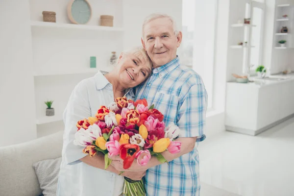 Photo of two adorable aged people hugging pair anniversary holiday surprise big red tulips bunch flat indoors