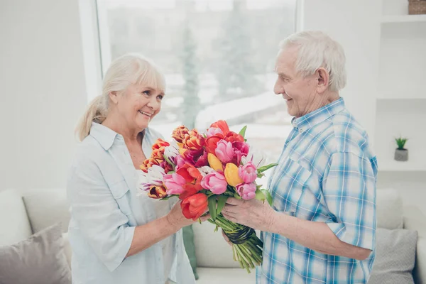 Foto de perfil de dos personas de edad adorable par lindo aniversario vacaciones sorpresa grandes tulipanes rojos manojo brillante plana en el interior —  Fotos de Stock