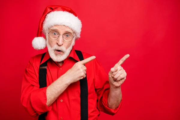 Close-up portret van zijn hij mooi verbaasd verbaasd verwonderd bebaarde Kerstman wijzend twee wijsvingers opzij ad kopie ruimte geïsoleerd over helder levendige glans levendige rode achtergrond — Stockfoto