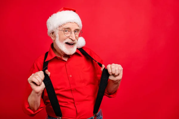 Close-up portret van zijn he nice trendy grappig vrolijk vrolijk blij bebaarde Kerstman trekken bretels plezier geïsoleerd over helder levendige glans levendige rode achtergrond — Stockfoto