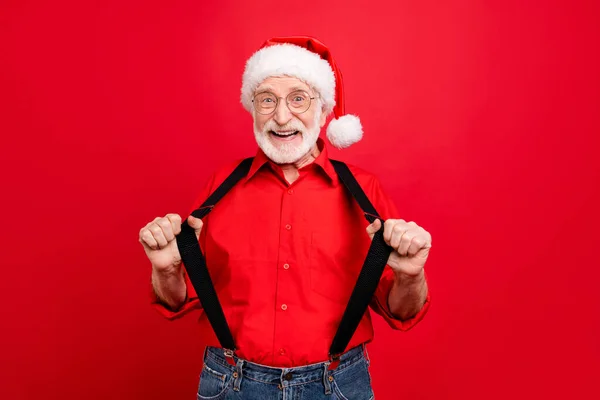 Portret van zijn hij mooie trendy vrolijke vrolijk blij opgewonden bebaarde kerstman trekken bretels geïsoleerd over heldere levendige glans levendige rode achtergrond — Stockfoto
