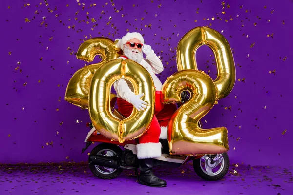 Фотографія повного тіла товстого Санта чоловіка, що сидить на велосипеді, тримає велике повітря новорічні кульки 2020 року, конфітті, що падають, одягнені в сонце специфікації рентгенівського костюма ізольовані фіолетовий фон — стокове фото