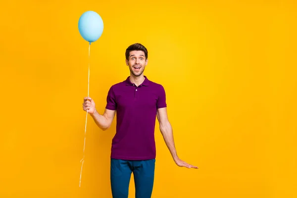Foto de alegre hombre guapo casual positivo sosteniendo la bola de aire de helio con las manos usando pantalones pantalones azules aislados sobre un fondo de color vivo —  Fotos de Stock