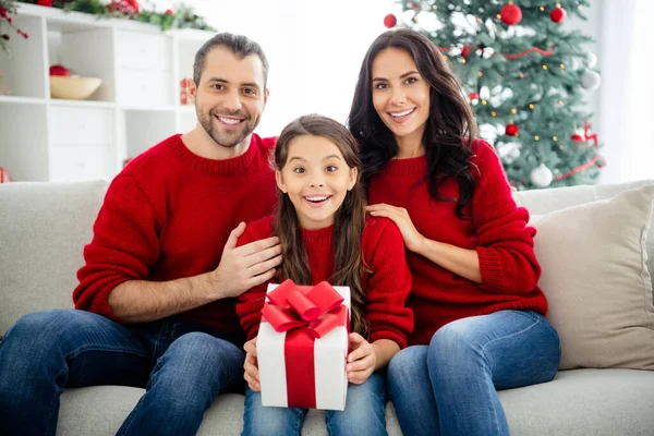 Portrait of three nice attractive lovely delighted positive cheerful cheery glad family mommy daddy celebrating enjoying leisure sitting on divan in decorated light white interior room