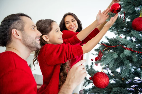 Profile side view portrait of three nice attractive lovely sweet charming cheerful cheery friendly family celebrating newyear christmastime leisure hanging fir in modern light white interior room Stock Picture