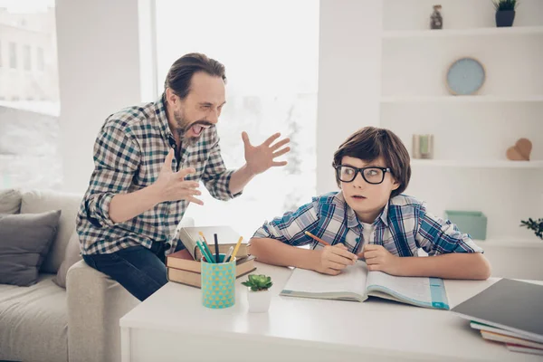 Photo of aggressive dad screaming at his small son who does not understand the material and home task he is very terrified sitting at the table trying to concentrate read textbook