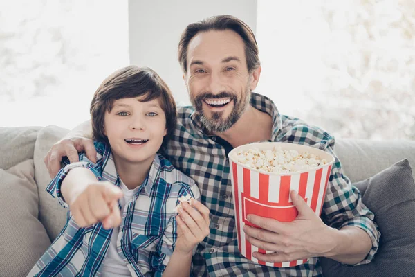 Las mejores vacaciones con concepto de mejor amigo. Foto de alegre padre loco emocionado abrazando abrazando a su linda descendencia disfrutando de un programa de comedia en la televisión comiendo bocadillos — Foto de Stock