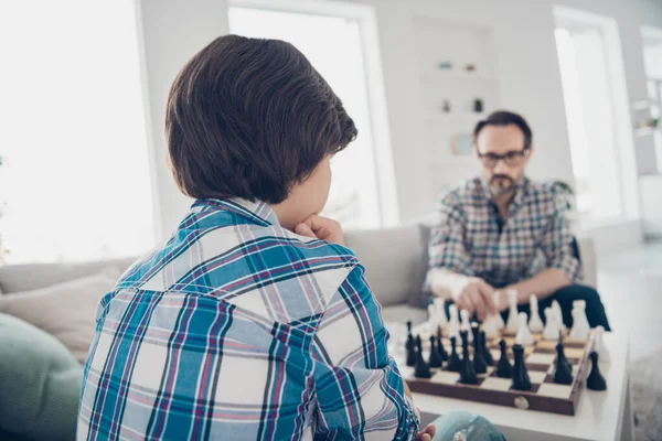 Portré két jól képzett, koncentrált, komoly fickóról apa és tinédzser fiú ül a kanapén, sakkoznak, mozgó darabokat játszanak a világos fehér, modern belső házban. — Stock Fotó