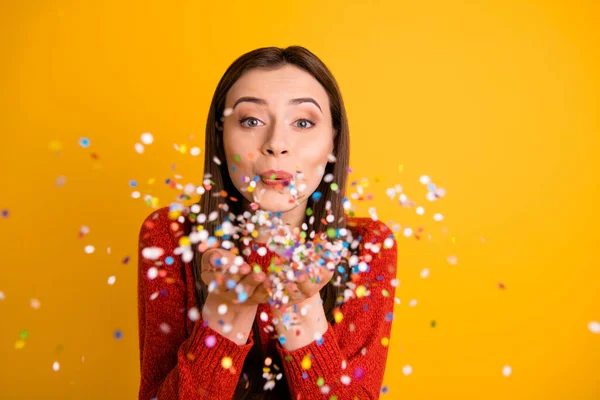 Foto van lief schattig leuk vrolijk fascinerend meisje blazen confetti met lippen weggevreten uit haar handen geïsoleerd over geel levendige kleur achtergrond — Stockfoto