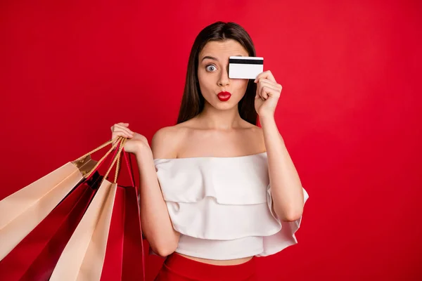 Retrato de adorable cara de piel de dama con tarjeta de crédito sosteniendo bolsas brillantes vestidos de blanco fuera de hombros aislados sobre fondo rojo — Foto de Stock