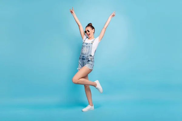 Ganzkörpergröße Foto von chilling dancing walking girl careless wearing jeans denim Overall zeigt jeder V-Zeichen, während isoliert mit blauem Hintergrund — Stockfoto