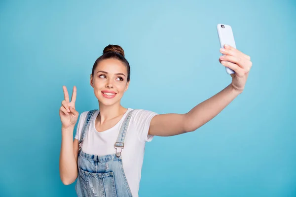 Foto de alegre hermosa chica bonita atractiva que le muestra v-signo de usar jeans denim en general, mientras que aislado con fondo azul — Foto de Stock