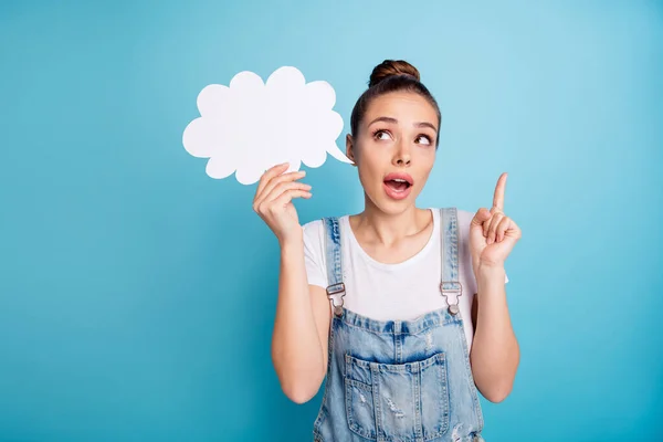 Retrato de impressionado linda menina mostrando seu dedo indicador segurando bolha de cartão de papel vestindo branco t-shirt jeans jeans macacão isolado sobre fundo azul — Fotografia de Stock