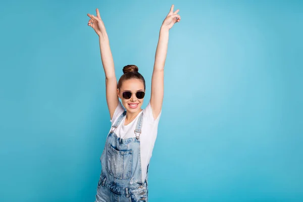 Retrato de chica divertida funky con anteojos gafas levantando v-signos que llevan camiseta blanca vaqueros overoles aislados sobre fondo azul — Foto de Stock