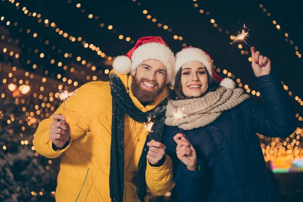 Foto do casal cara senhora duas pessoas no x-mas celebração no parque segurando faíscas mágicas ao ar livre festa do ano novo vestindo casacos quentes santa tampas lenços luvas — Fotografia de Stock