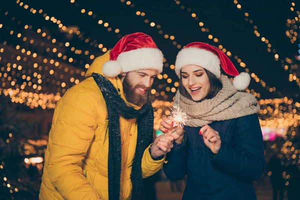 Komik bir çift fotoğrafı, bayan. Yılbaşı parkında ateş büyüsü yapan iki kişi. Yeni yıl partisinde dışarıda sıcak paltolar giyip Noel Baba şapkası eldivenleri takıyorlar. — Stok fotoğraf