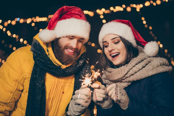 Karı-koca fotoğrafı. Parktaki Noel kutlamasında elinde sihirli maytaplar olan iki kişi. Yeni yıl partisinde, kalın paltolar giyip Noel Baba şapkası eldivenleri takıyor. — Stok fotoğraf