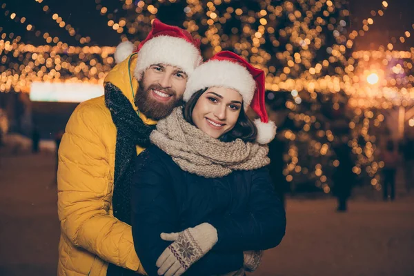 メリークリスマス2人の男の女性の写真は、都市を訪問ライトアップされた公園を訪問夏の夜霜天気スタンドピギーバックは冬のジャケットスカーフサンタ帽子を屋外で着用 — ストック写真