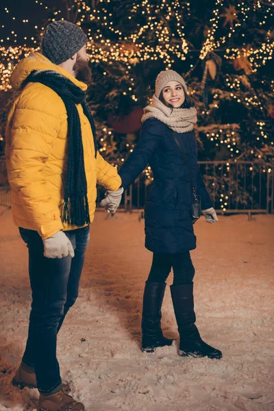 Повна довжина вертикальна фотографія двох людей хлопець леді ходить вогні міський парк новорічний вечір насолоджуватися кращою компанією морозної погоди одягати зимові куртки шарфи капелюхи на відкритому повітрі — стокове фото