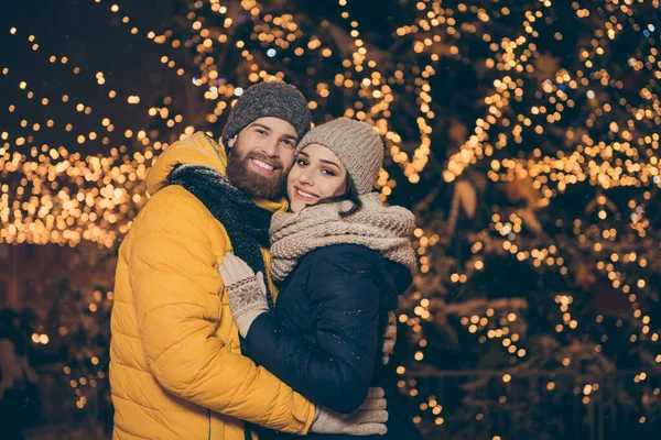 Foto von zwei Personen Paar Kerl Dame umarmen Besuch Stadt beleuchtet Park Neujahr Nacht frostiges Wetter stehen in der Nähe tragen Winterjacken Schals Mützen Handschuhe im Freien — Stockfoto