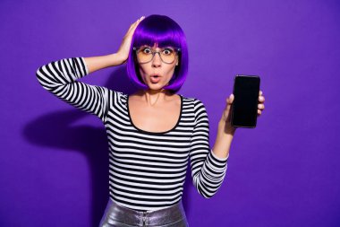 Portrait of puzzled millennial touch head with hand holding modern technology isolated over violet purple background clipart