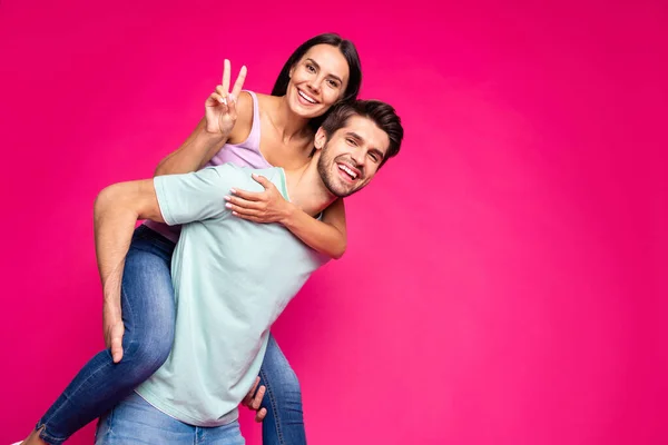 Foto von lustigen sorglosen Kerl und Dame hält Huckepack zeigt V-Zeichen Symbol tragen lässige Kleidung isoliert lebendige rosa Farbe Hintergrund — Stockfoto