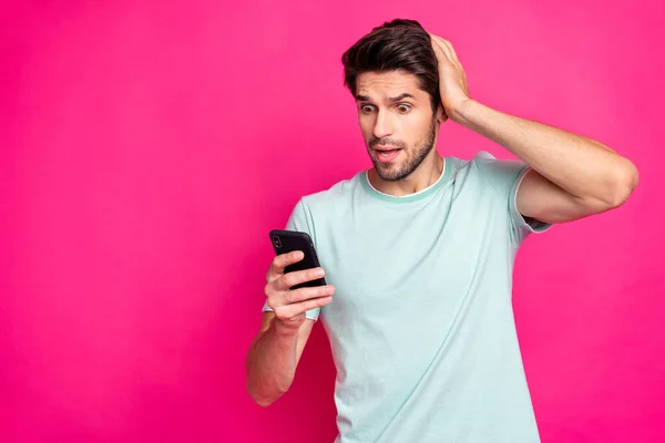 Photo of blogger guy holding telephone in hands checking subscribers noticed many unfollowers wear casual outfit isolated vivid pink color background