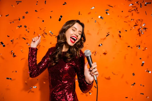 Retrato de positivo alegre menina cantar música desfrutar de despedida de solteiro evento divirta-se segurar microfone desgaste elegante luxo roupa isolada sobre cor laranja fundo serpentina voando — Fotografia de Stock