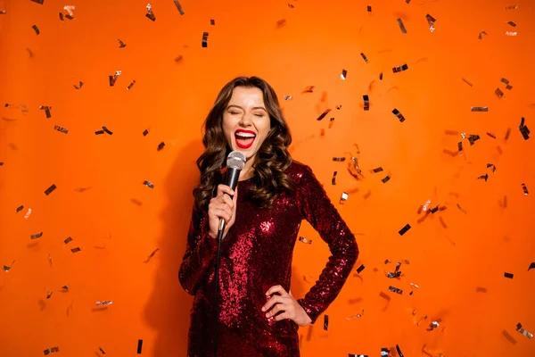 Retrato de chica soltera encantadora tienen fiesta de graduación evento cantar canción sostener micrófono sentir diversión usar ropa elegante de lujo aislado sobre fondo de color naranja serpentina caída —  Fotos de Stock