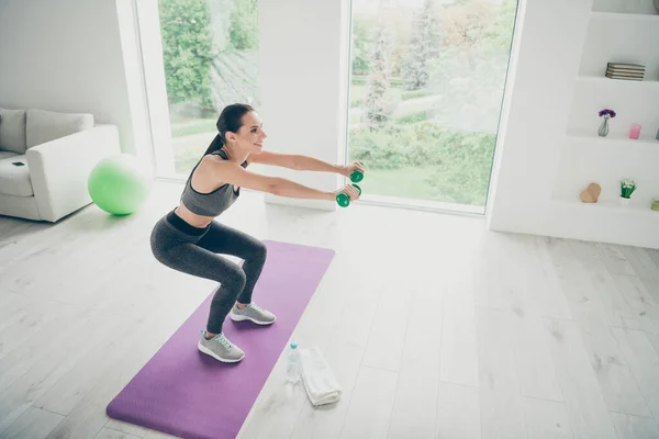 Top nad vysokým úhlem fotografie aktivní sportovkyně profil vedlejší praxe sportovní gymnastika, aby squaty držet zelené činky nosit moderní sportovní kalhoty ve fitness studiu — Stock fotografie