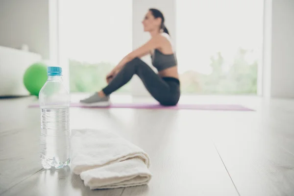 Foto de cerca de la botella de plástico con agua y mesa blanca sportawoman utilizará después de su calentamiento para relajarse se sienta en el lado del perfil de la alfombra púrpura en el gimnasio aeróbicos estudio — Foto de Stock