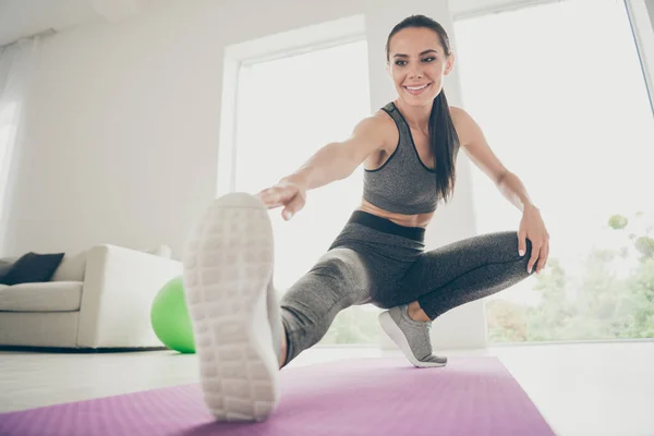 Foto em tamanho completo de alegre atleta ativa menina quer ser forte esportista prática aeróbica aquecimentos sentar-se no tapete violeta do agachamentos esticar as pernas tocar os dedos pé em casa como estúdio de fitness — Fotografia de Stock