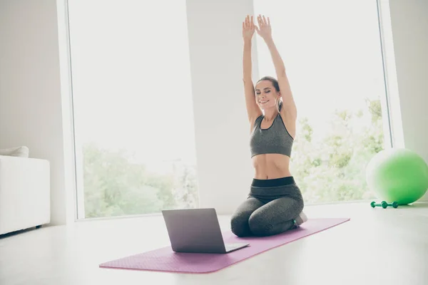 Full length photo of sportive woman watching daily tv sport channel for girls want be slim do cross fitness άσκηση τεντώστε τα χέρια αισθάνονται ειρηνικά κάθονται σε μωβ ματ στο γυμναστήριο-όπως το σπίτι — Φωτογραφία Αρχείου