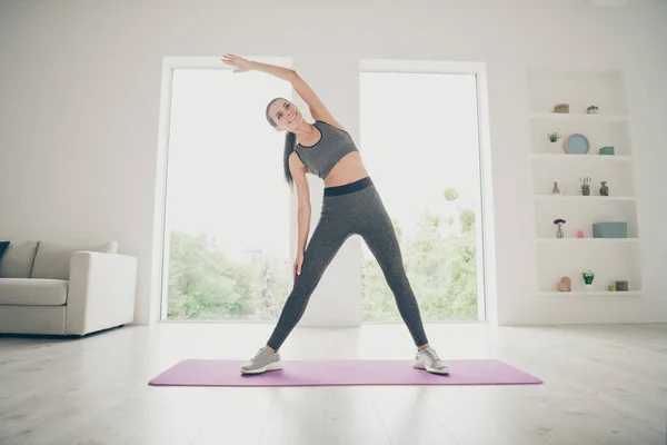 Longitud completa tamaño del cuerpo foto de alegre lindo agradable encantadora mujer deportiva estiramiento de pie en la alfombra —  Fotos de Stock