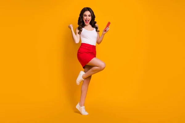 Foto de perfil de tamaño completo de la señora divertida boca abierta teléfono leer blog levantar el puño ganar sorteo regalo regalo regalo ropa casual blanco tanque-top rojo falda zapatos aislados de color amarillo fondo — Foto de Stock