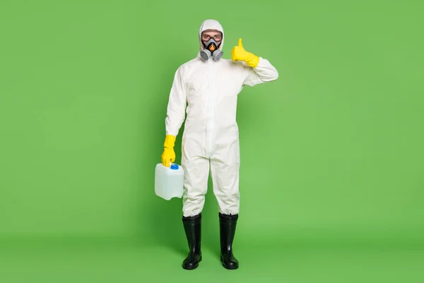 Foto de longitud completa de seguro de éxito chico trabajador médico limpiador mantenga botella botella botella química parada covid mostrar pulgar hacia arriba desgaste de látex blanco hazmat uniforme aislado color verde fondo — Foto de Stock