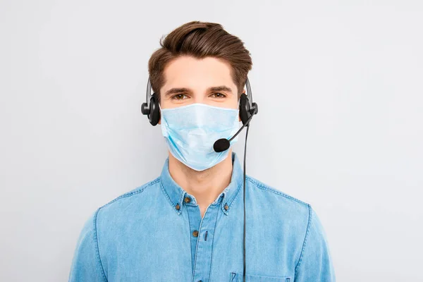Portrait of young man worker of call center assistance wear medical mask on face and headset with microphone help other people isolated on gray background, stop pandemic of corona virus concept