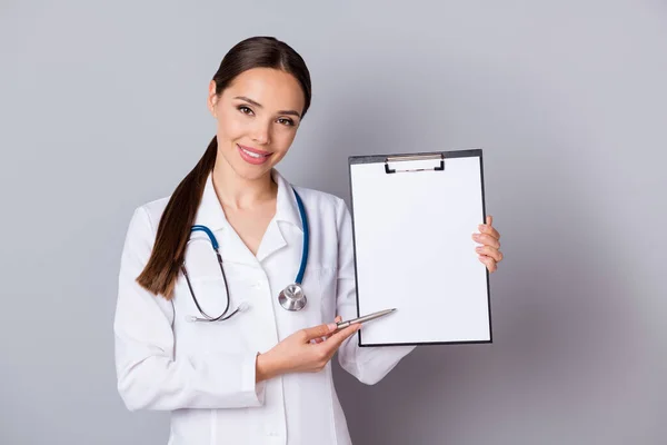 Фото красивої професійної докторантки, що показує місце пацієнта для підписання договору страхування клініки, носить стетоскоп біле лабораторне пальто ізольоване сіро-кольорове тло — стокове фото