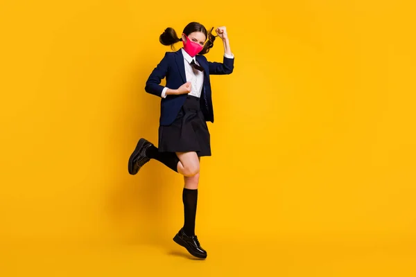 フル長さの写真の高校生の女の子ジャンプ上昇拳着用黒ジャケットブレザー長いソックススカート医学マスク絶縁以上明るい輝き黄色の色の背景 — ストック写真