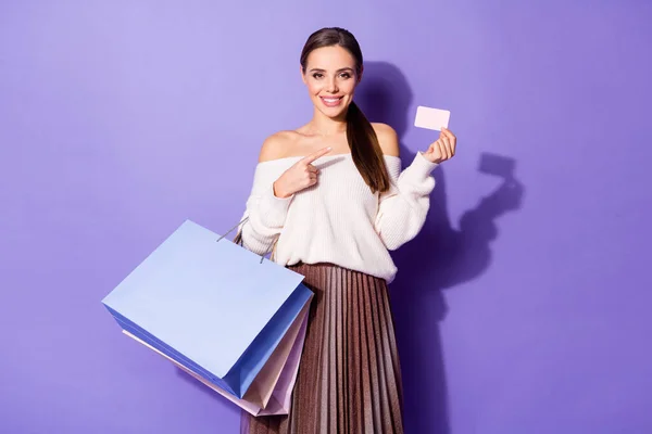 Positief vrolijk meisje winkelcentrum klant punt index vinger wit papier kaart geven aan dat ze kan betalen pakketten dragen off-schouder wit trui rok geïsoleerde violet kleur achtergrond — Stockfoto