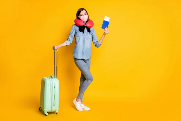 Foto de tamaño completo de estudiante niña bolsa de mano maleta billetes de viaje listo en el extranjero llevar máscara médica cuello cojín vaqueros camisa de vaqueros aislados sobre fondo de color amarillo —  Fotos de Stock