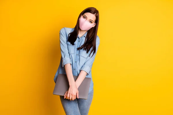 Portrait de fille positive dans un masque médical tenir ordinateur portable profiter de travail à distance porter casual jeans chemise isolée sur fond de couleur brillante — Photo