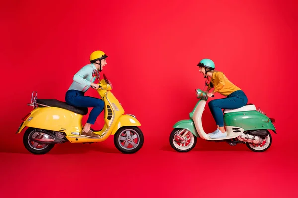 Profil vue de côté de agréable attrayant fou joyeux joyeux couple joyeux conduite cyclomoteur en face de l'autre avoir du plaisir isolé sur brillant vif fond de couleur rouge vif — Photo