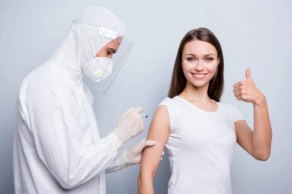 Photo of young positive patient lady guy expert doc inject shoulder covid antidote vaccine girl raise thumb up wear mask hood uniform plastic facial protection isolated grey color background — Stock Photo, Image